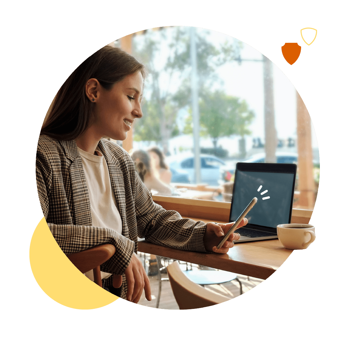 Une femme consulte son téléphone dans un café devant son ordinateur portable